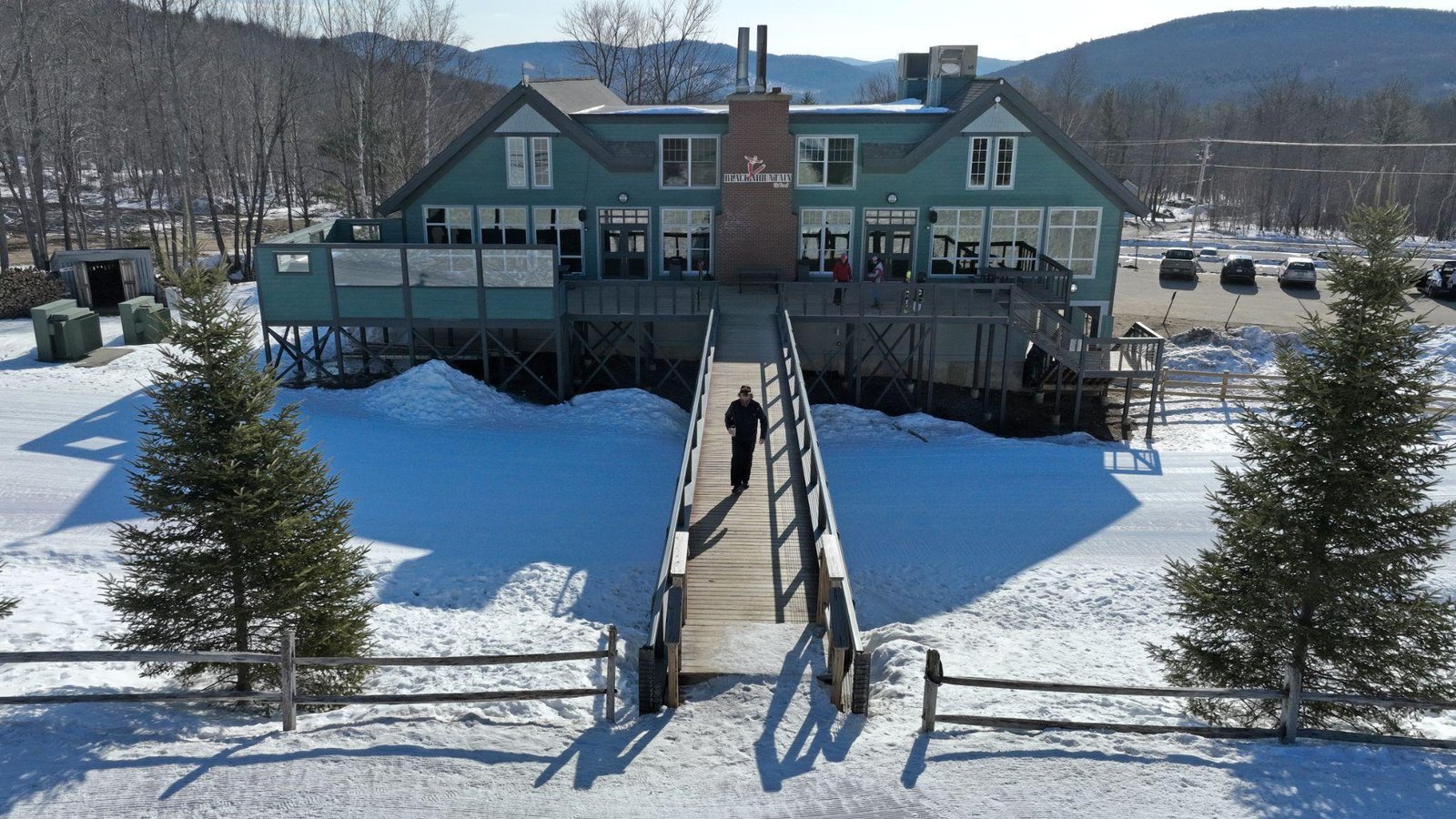This photo shows an aerial view of a house with a bridge in front of it and snow around it.