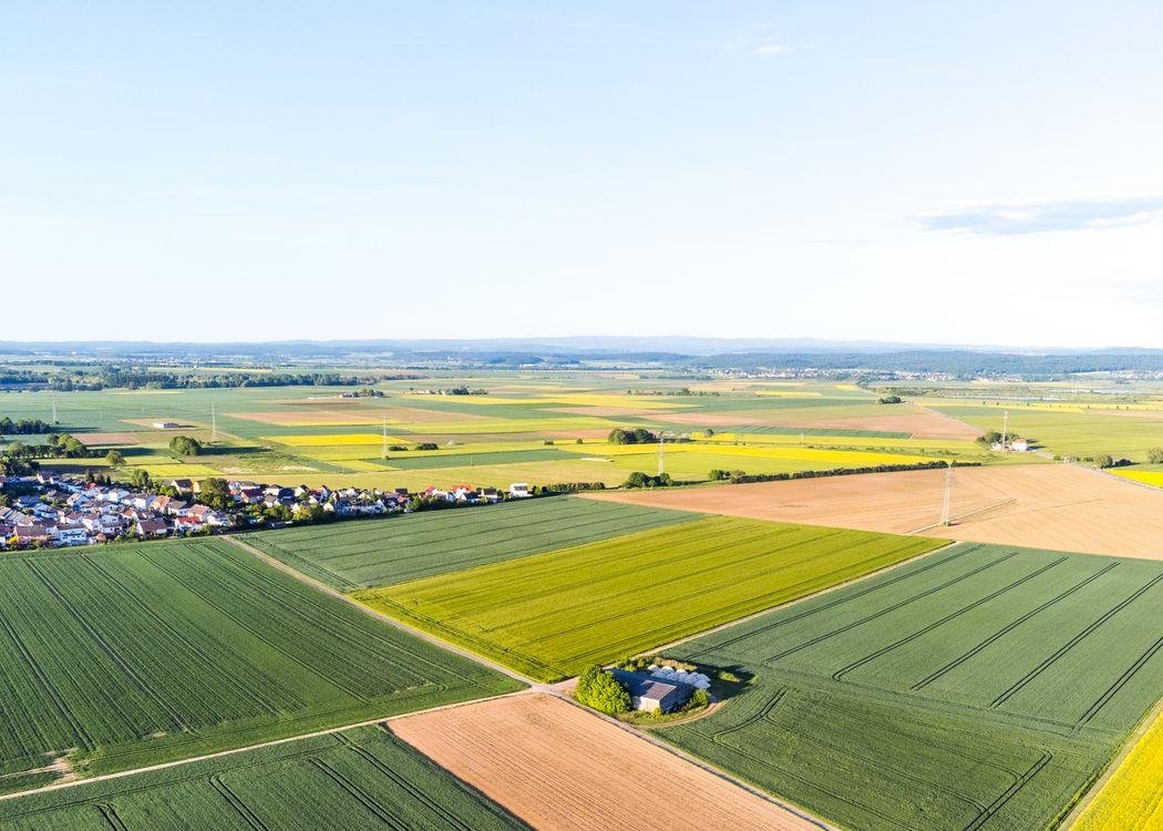 Aerial drone view of vast agricultural fields with varied crops and a small rural community.