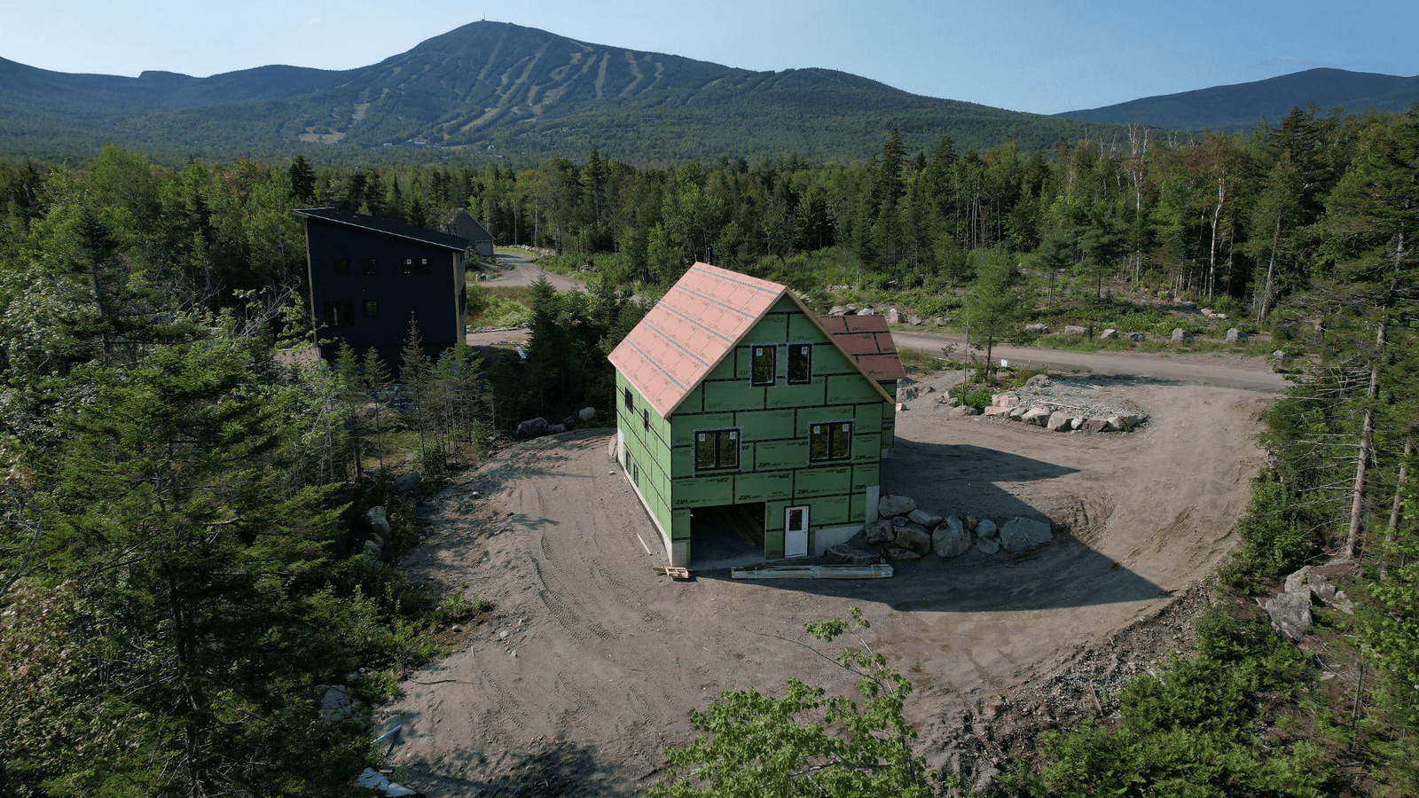 Aerial drone view of a residential building under construction on a cleared site with a ski mountain in the background in Maine.