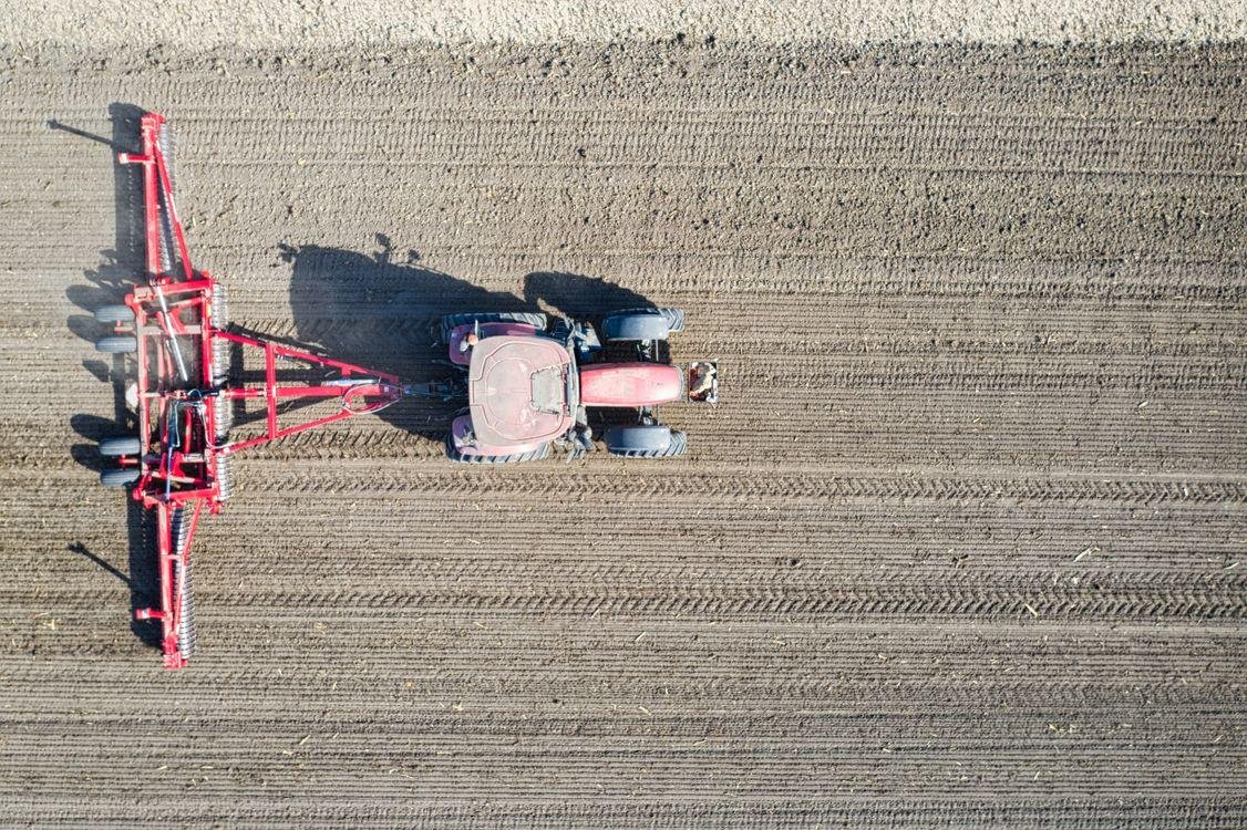 Aerial drone view of a tractor with seeding equipment working through a freshly tilled field.