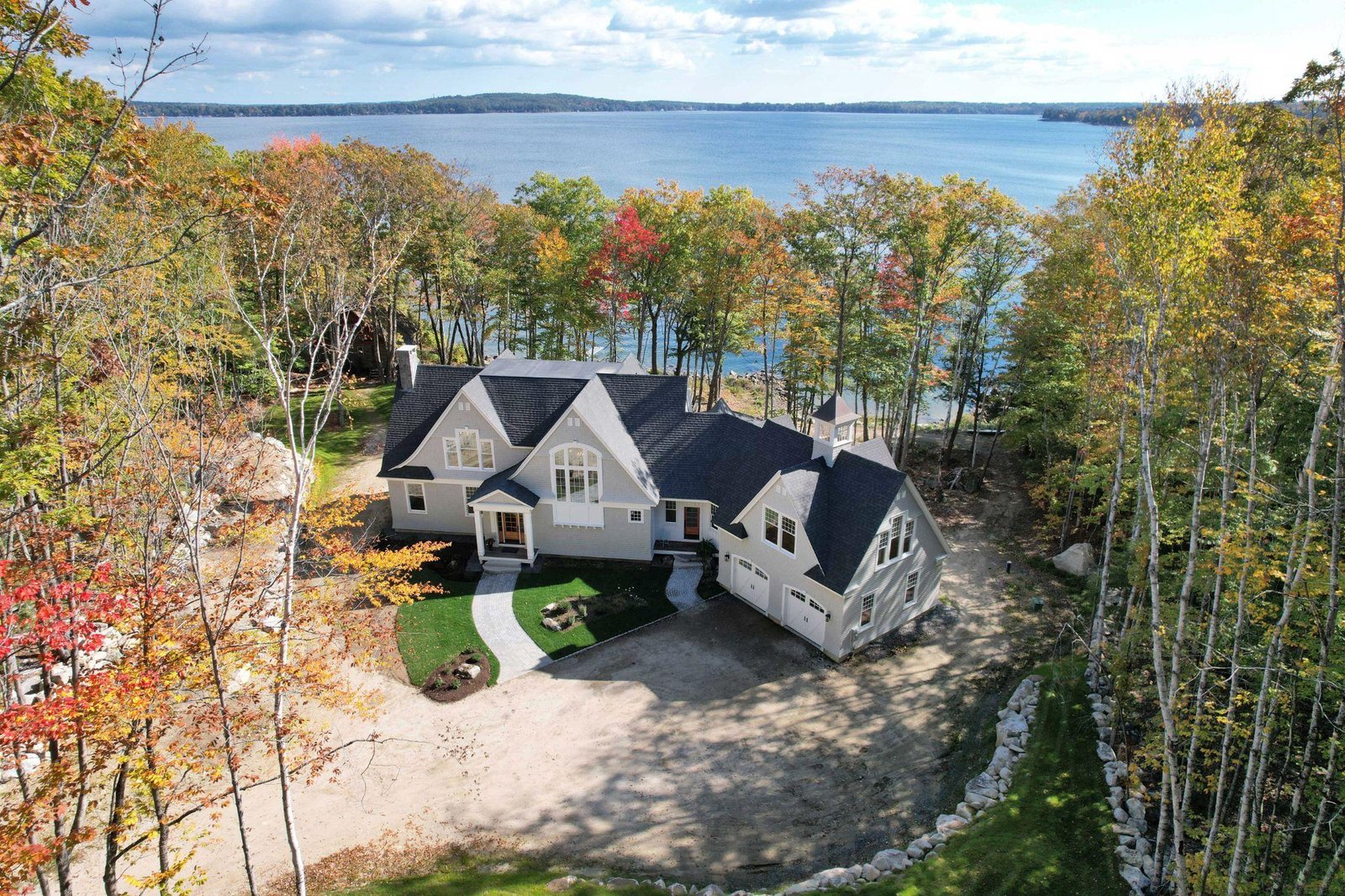 Aerial drone view of a luxury waterfront home surrounded by autumn foliage on a lake in Windham, Maine.
