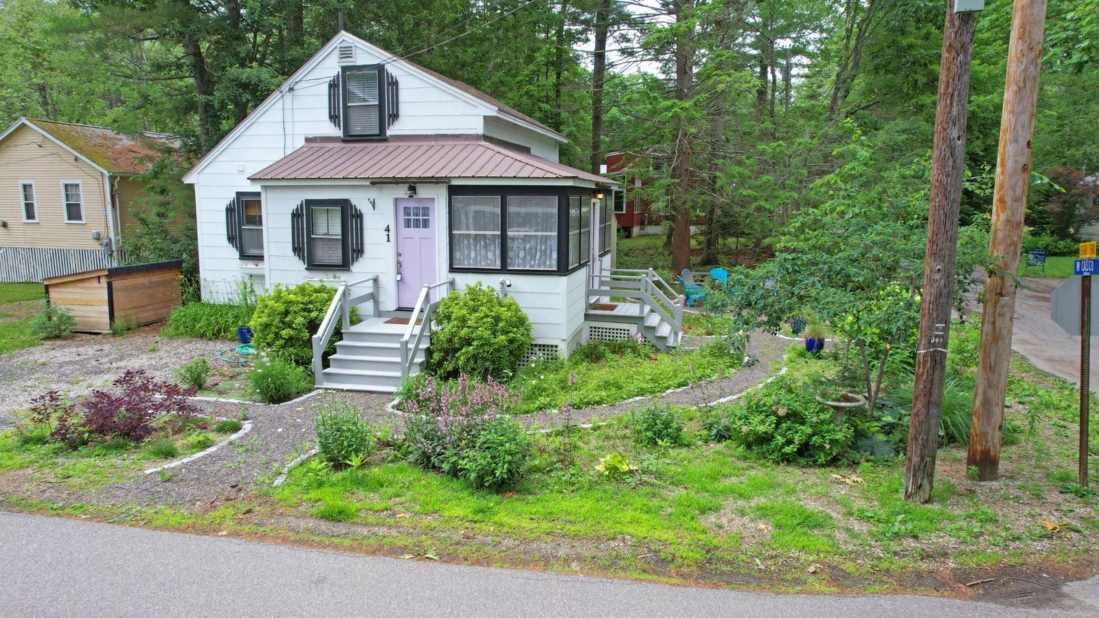 Low-angle drone view of a charming residential cottage with a landscaped garden corner lot in Old Orchard Beach, Maine.